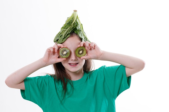 Girl posing with sliced kiwis blocking eyes and lettuce leaf on head