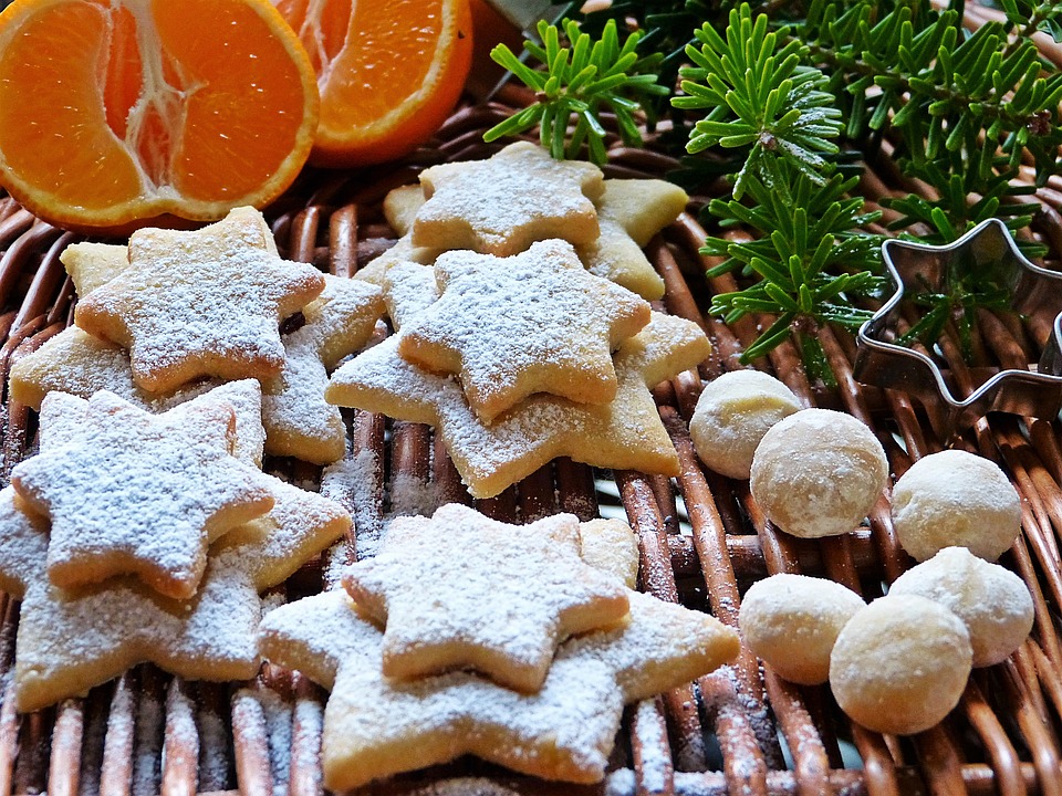 Christmas cookies in the shape of stars, with oranges and evergreens in the background